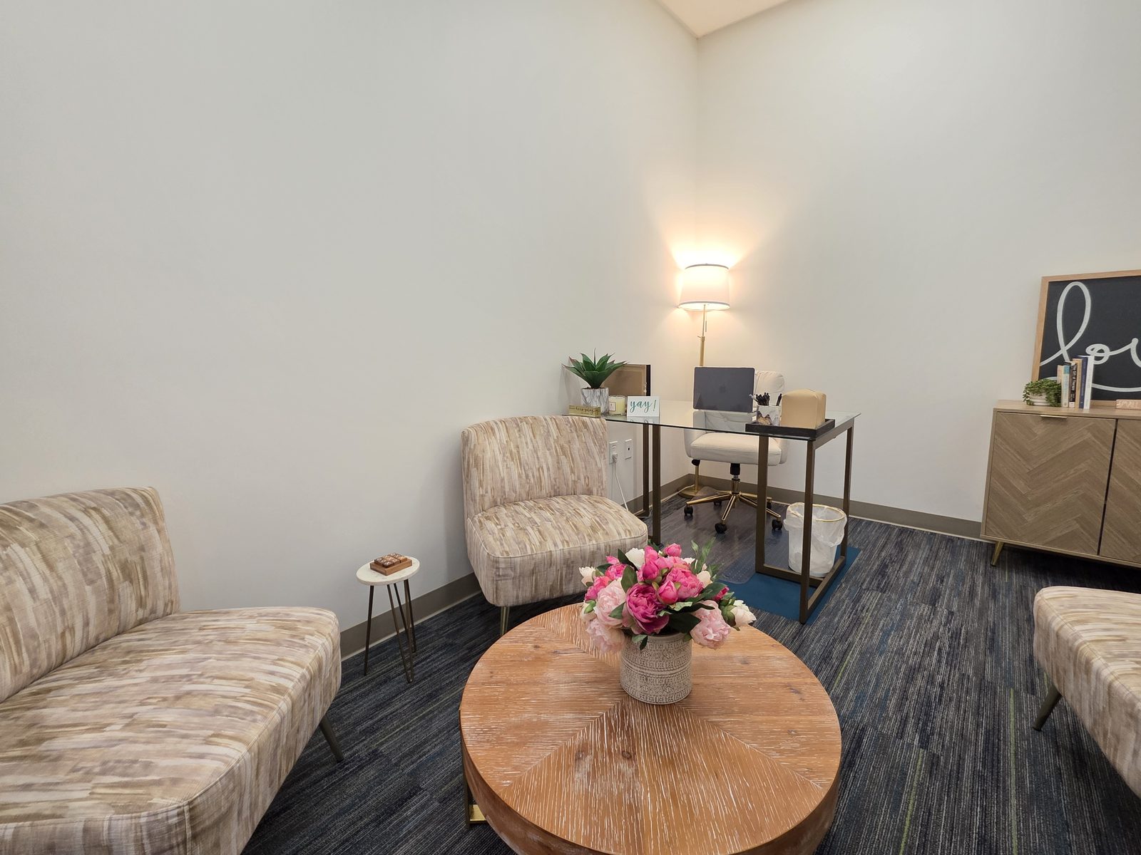 An individual therapy room with soft armchairs, a round wood table with fresh flowers, and warm lamplight
