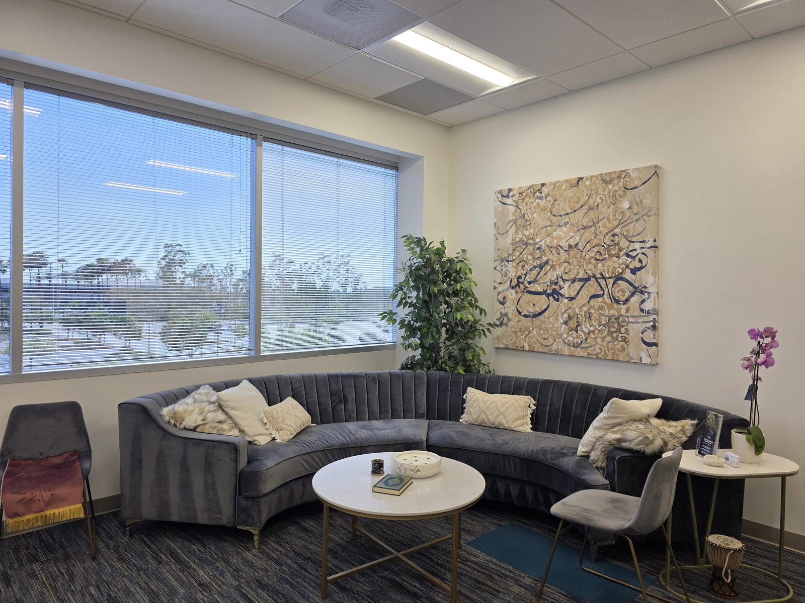 The Rahma Counseling waiting lounge — a curved sofa beneath Arabic calligraphy art, with a window overlooking palm trees