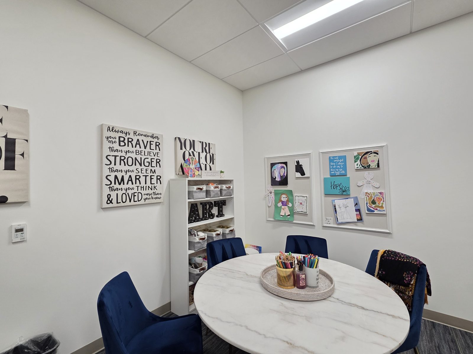 A youth art therapy room with a round marble table, art supplies, and children's artwork on the walls