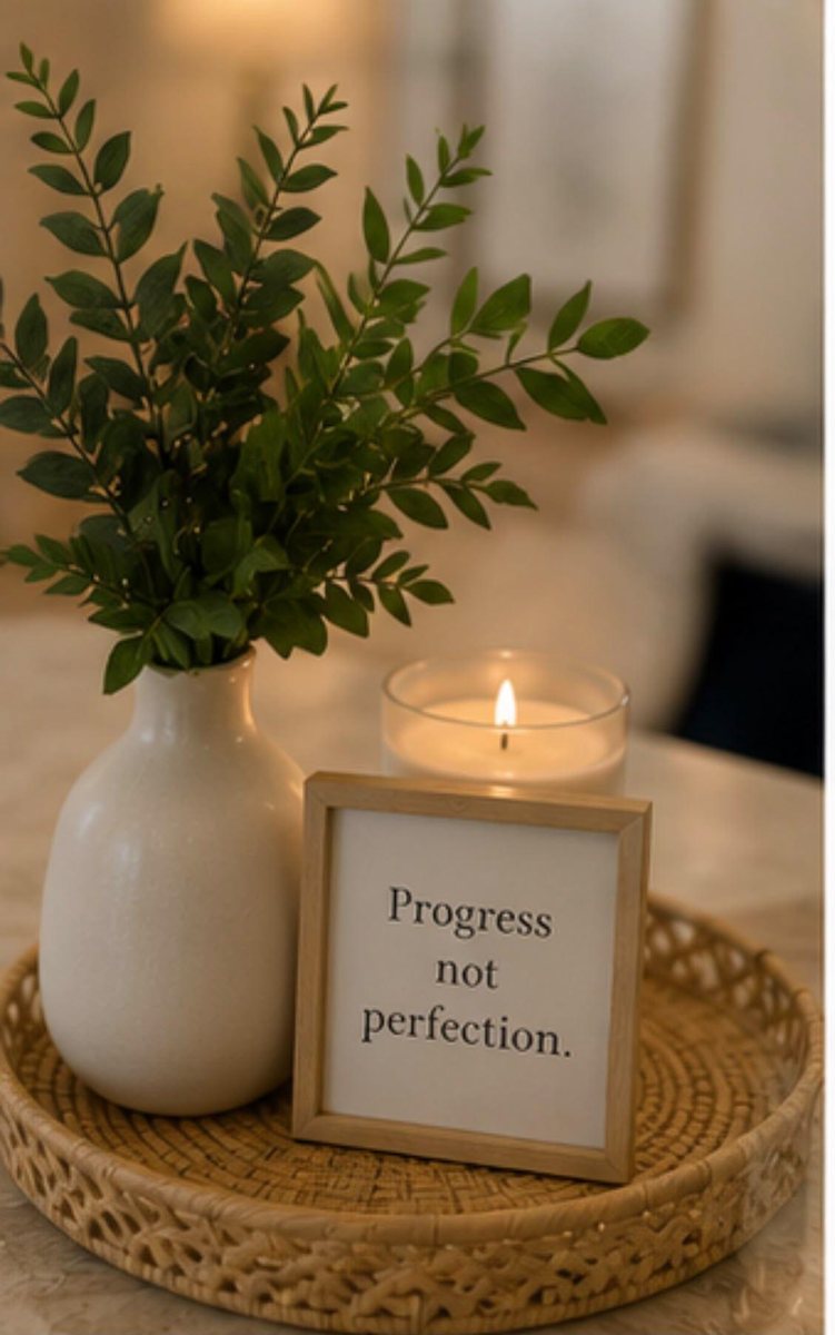 A framed sign reading Progress not perfection beside a candle and greenery